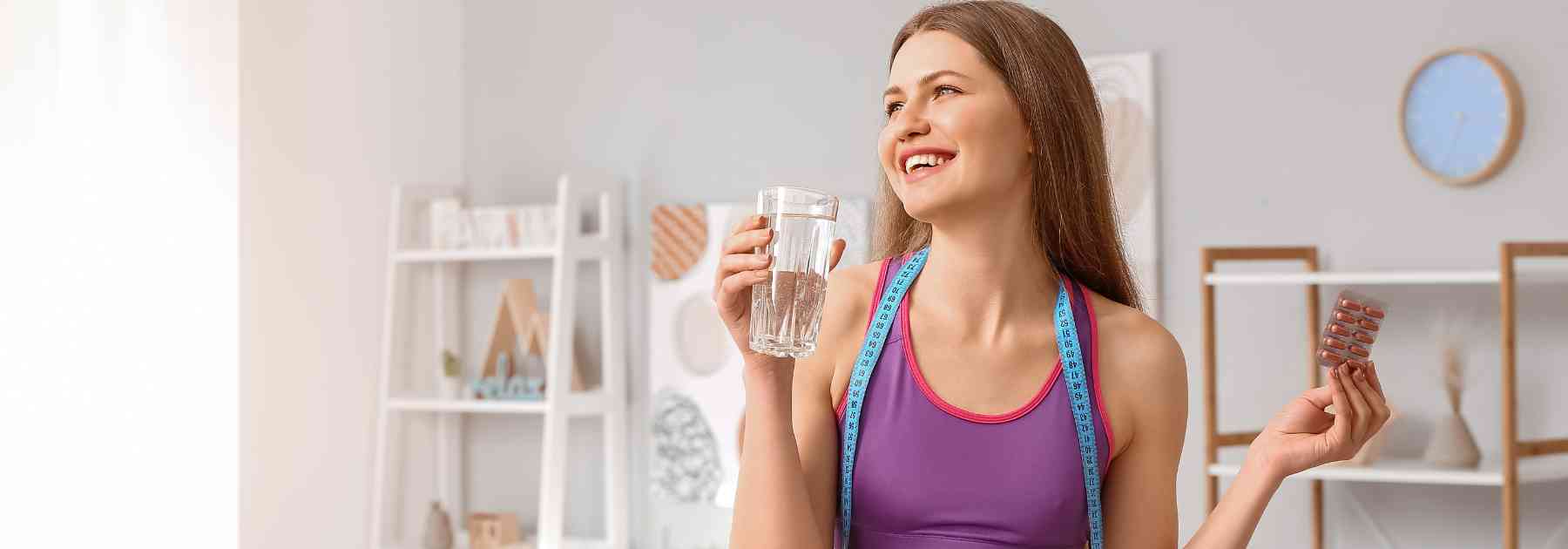 young woman smiling holding glass of water and supplements