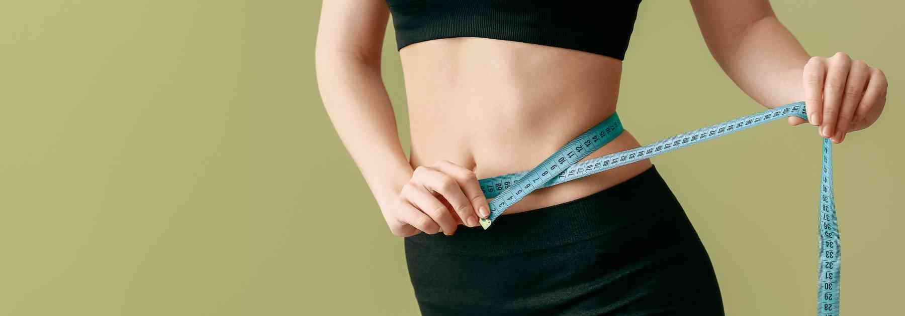 woman in workout gear measuring waist on green background