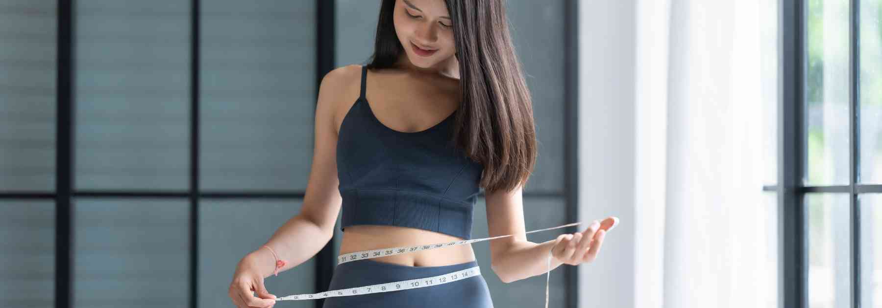 young woman in workout gear measuring waist