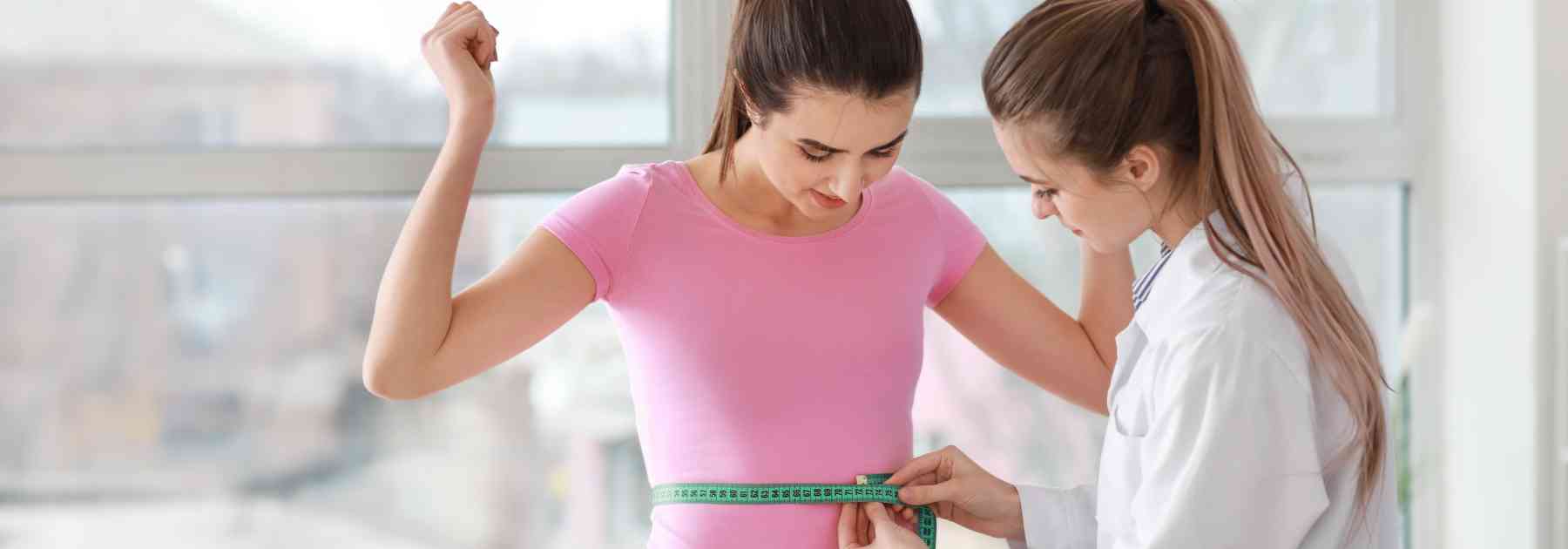 female patient having her waist measured by female doctor