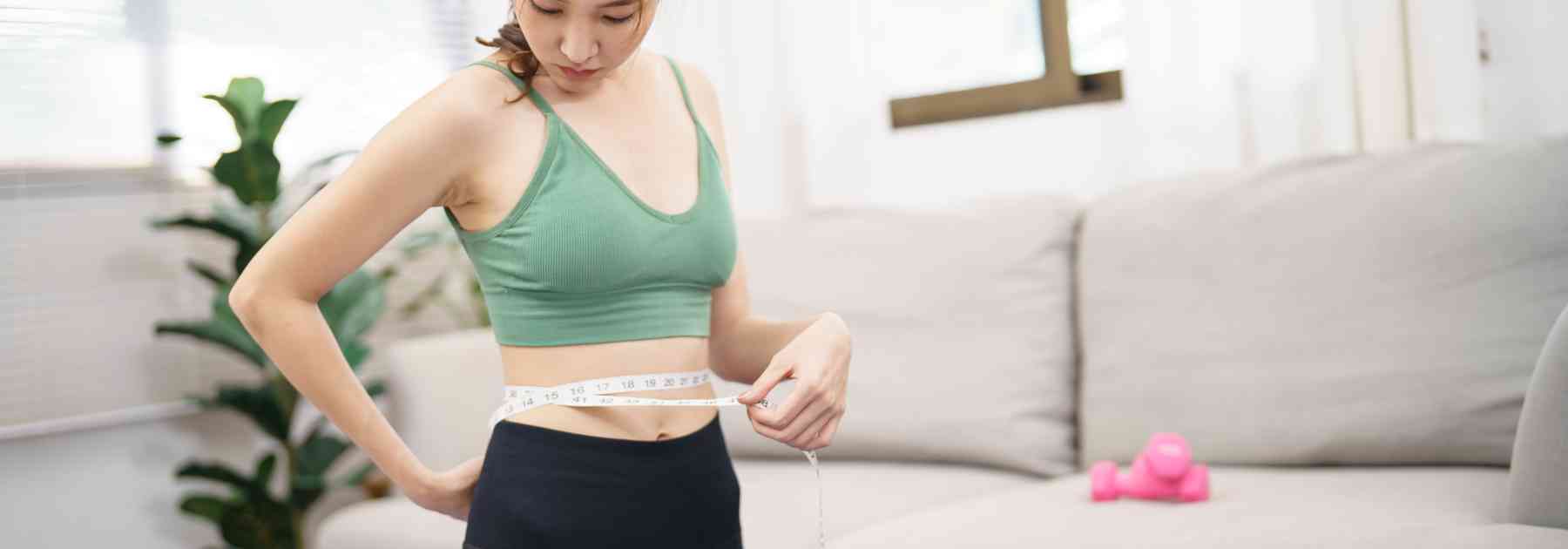 young woman in green crop top measuring her waist