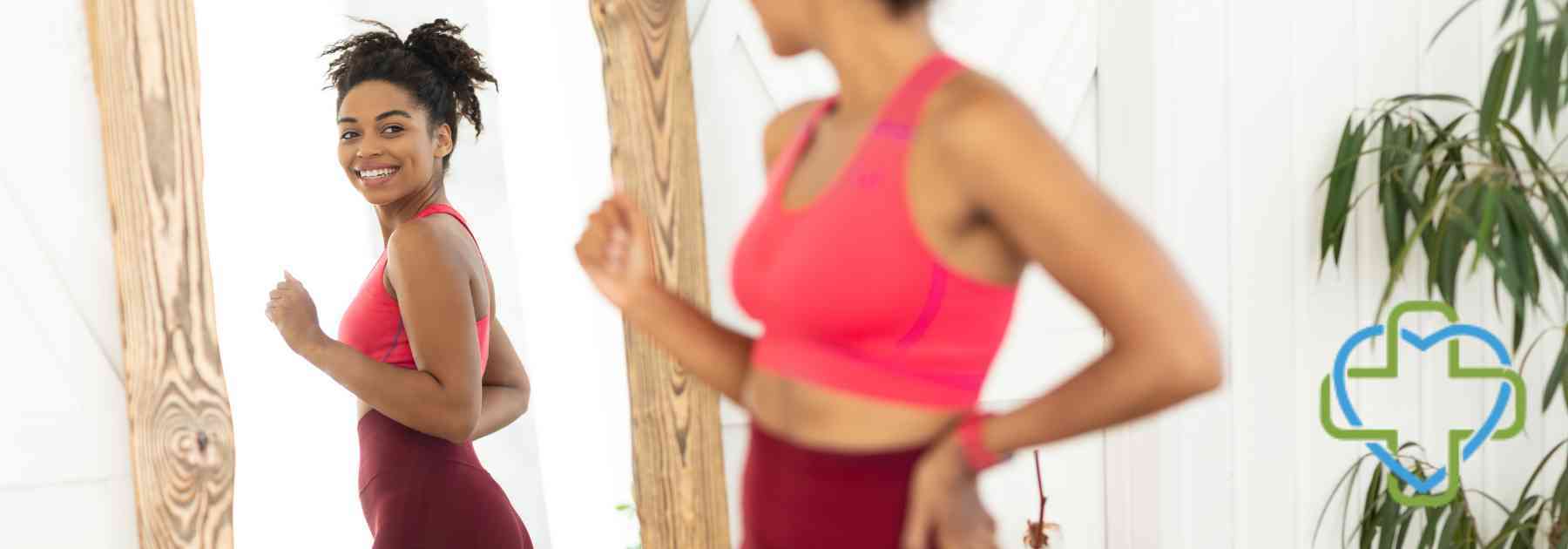 woman in workout gear smiling and looking in mirror