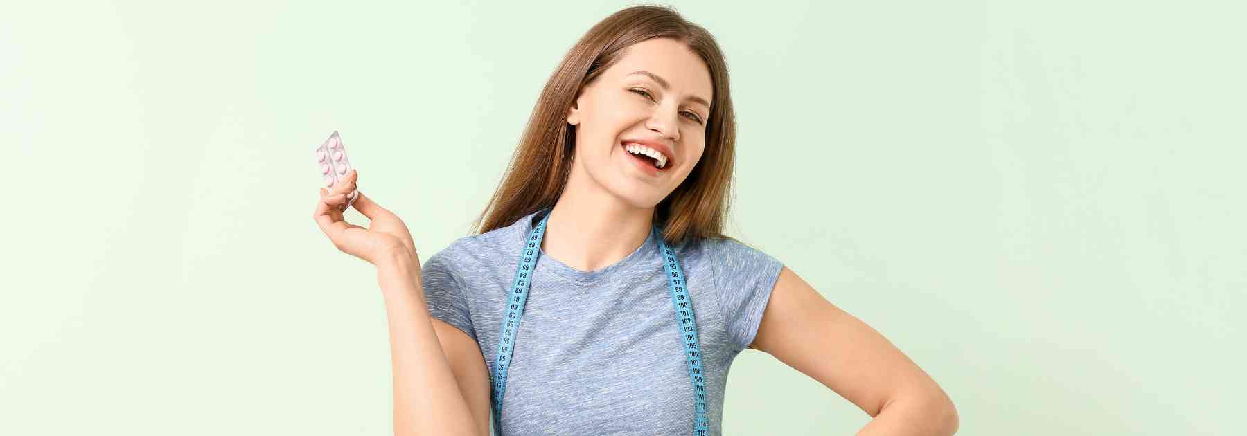 young woman smiling holding weight loss pills on green background