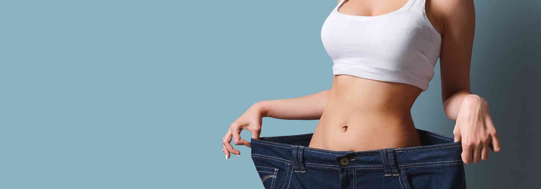 woman in white crop top wearing jeans too big on blue background