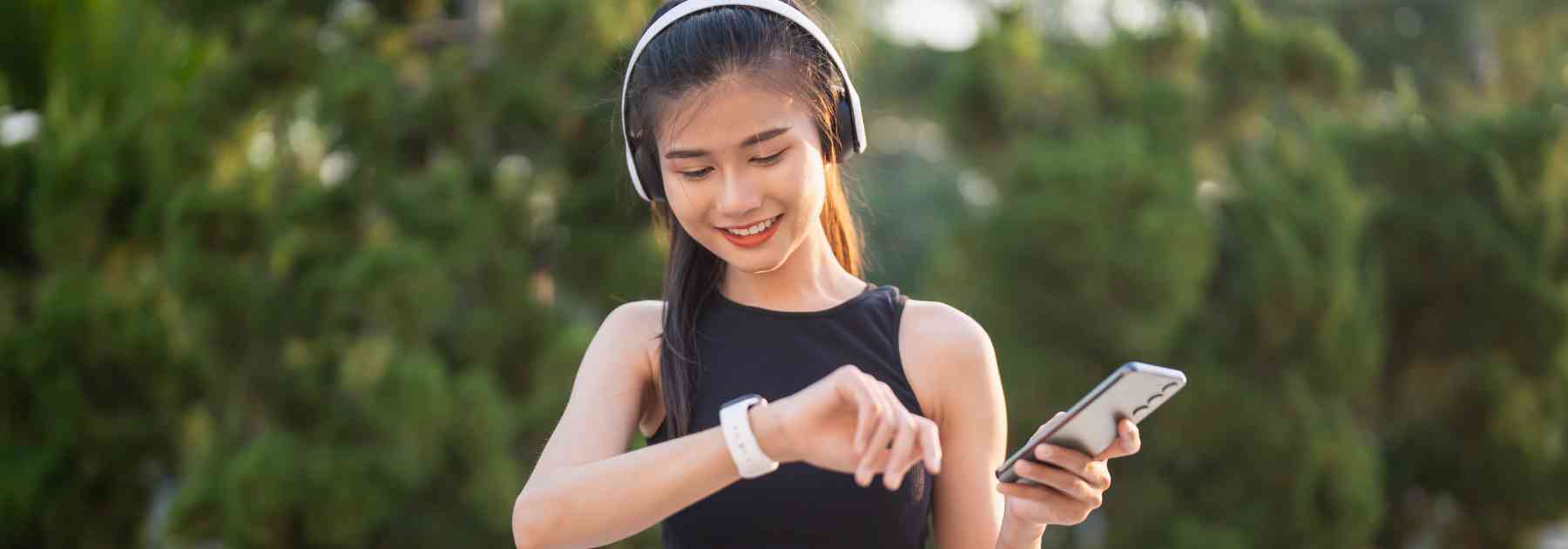 young woman wearing headphones checking smart watch smiling