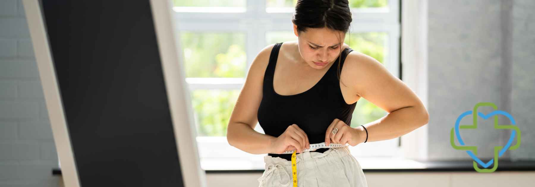 woman in workout gear measuring waist in front of mirror
