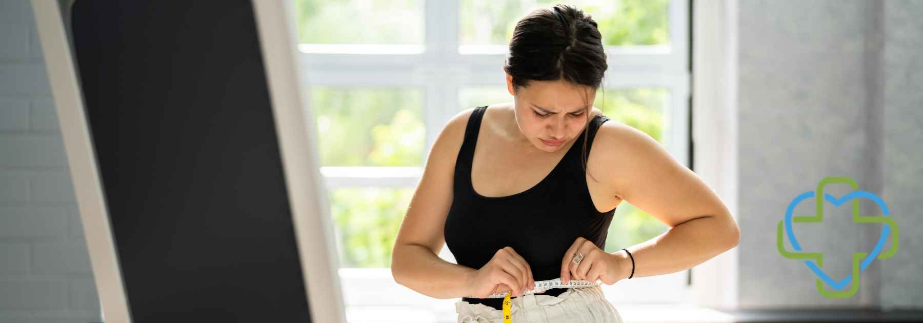 woman in workout gear measuring waist in front of mirror